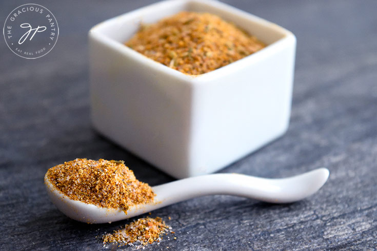 A horizontal image of adobo seasoning in a container and its matching spoon.