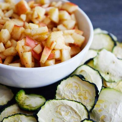 A small bowl of apple salsa sits surrounded by dehydrated zucchini chips. A tasty snack!