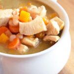 A white bowl filled with this Chicken Stew Recipe With Butternut Squash. You can see the chicken, carrots and bits of butternut squash sitting in a thickened broth.