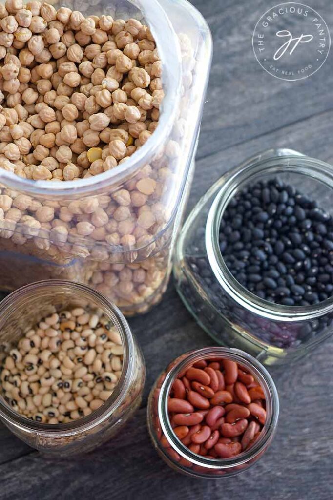 Containers of various beans sit with their lids off so you can see the beans in this guide to How To Cook Dry Beans.