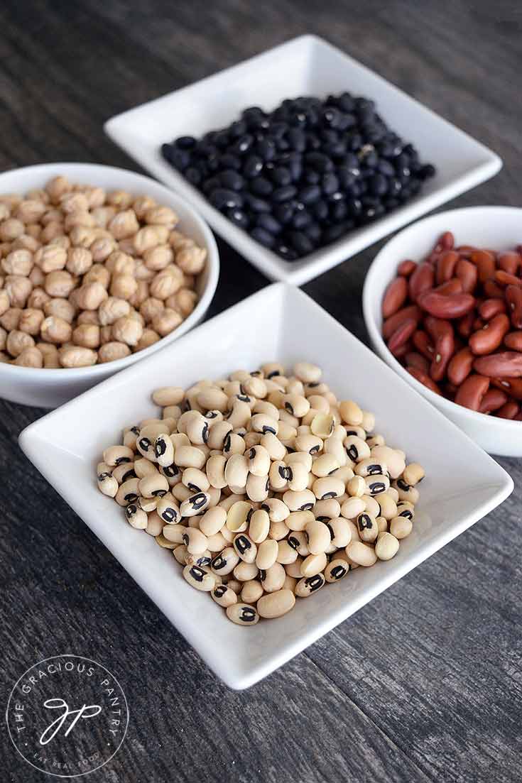 Four bowls sit with four different kinds of dry beans in them.