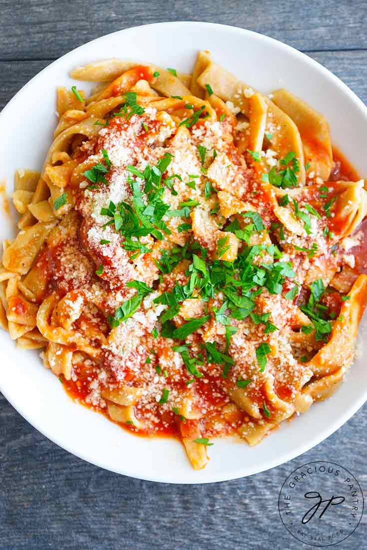 An overhead view of a freshly made bowl of pasta with red sauce and garnished with chopped herbs and parmesan cheese. Read more in this guide to How To Make Homemade Pasta.