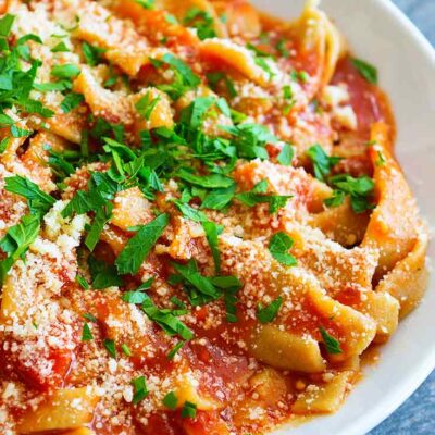 A beautiful bowl of fresh, homemade pasta sits garnished with parmesan and fresh parsley in this guide to How To Make Homemade Pasta.