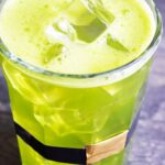 A glass wrapped with a leprechaun belt sits filled with this Green Lemonade Recipe.