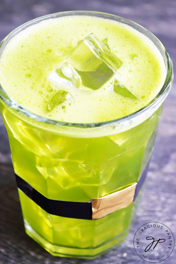 A glass wrapped with a leprechaun belt sits filled with this Green Lemonade Recipe.