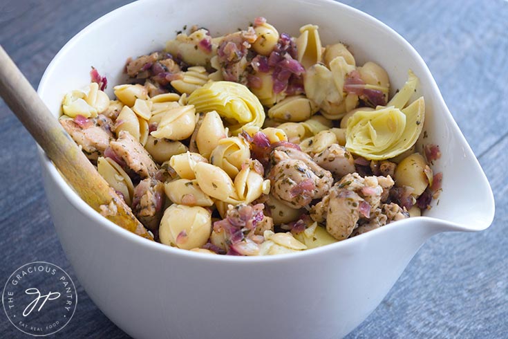 A side view looking just over the edge of a white serving bowl showing this artichoke chicken pasta.