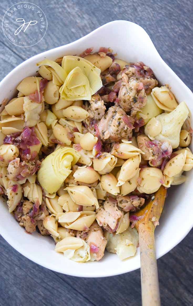 An overhead view looking down into a serving bowl of this delicious artichoke chicken pasta. A wooden spoon is in the bowl, ready to serve the pasta.