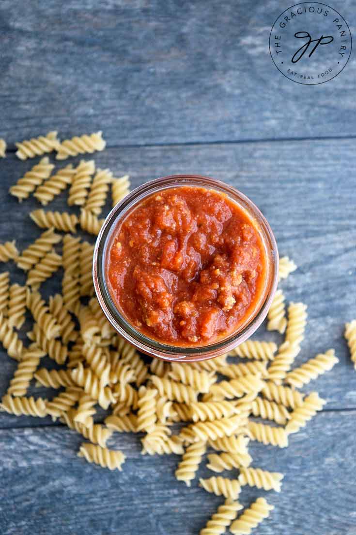 And overhead view of this homemade spaghetti sauce looking down into the open jar of sauce. Dry spiral pasta lays on the table at the base of the jar.