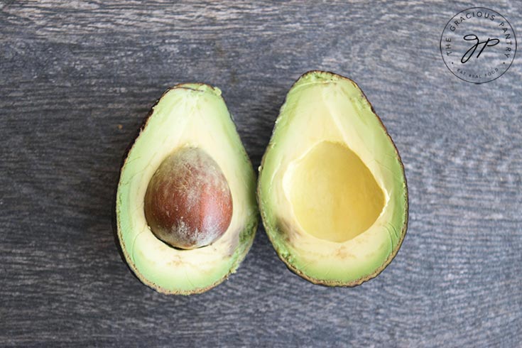 Cut avocado halves sit on a table. One side still has the seed in it.