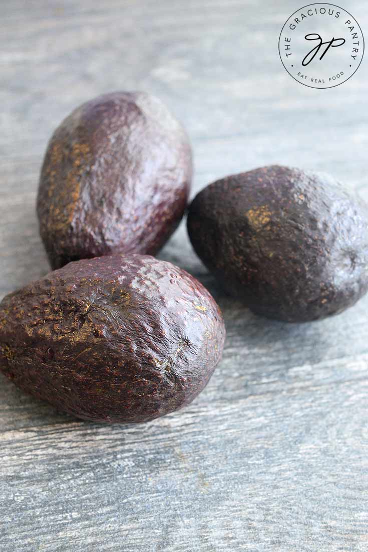 Three avocados sit on a table waiting to be prepped for the freezer in this guide to how to freeze avocados