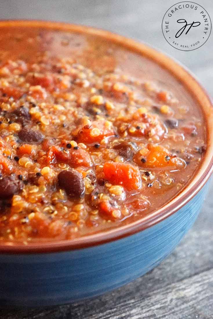 A blue bowl filled with this Quinoa Chili sits ready to eat. You can see the quinoa and black beans with bits of tomatoes.