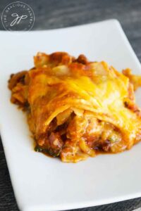 A square of this Homemade Lasagna Recipe sits on a white plate, showing off it's cheesy gooey-ness.