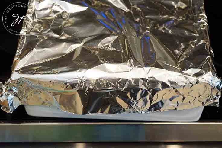 A lasagna covered in foil in the oven.
