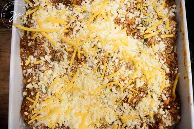 A layer of cheese sprinkled over sauce in a lasgna pan.