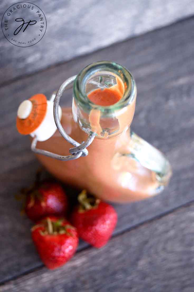 An overhead view of this bottle of Strawberry Balsamic Vinaigrette, looking down into the filled bottle. You can see fresh strawberries on the table at the base of the bottle.