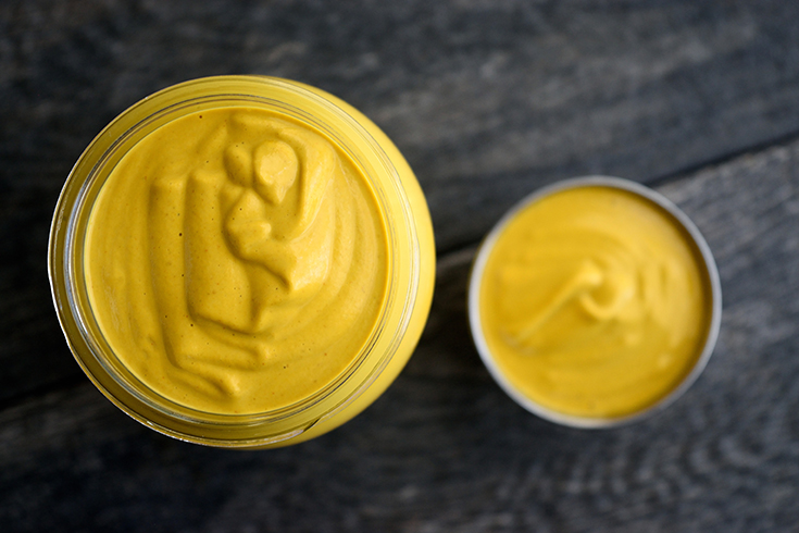 An overhead view looking down into an open jar and condiment container sitting next to each other, filled with this Vegan Cheese Sauce.