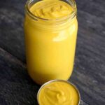 A small condiment container sits in front of an open jar. Both are filled with this Vegan Cheese Sauce.