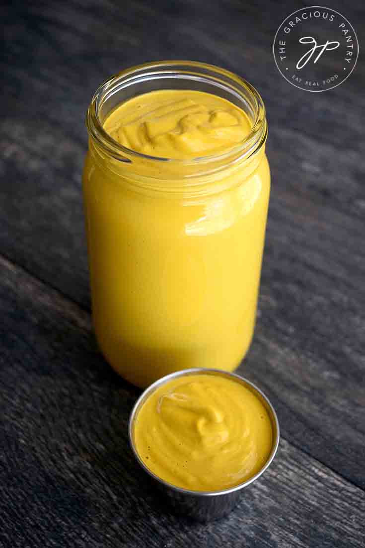 A small condiment container sits in front of an open jar. Both are filled with this Vegan Cheese Sauce.