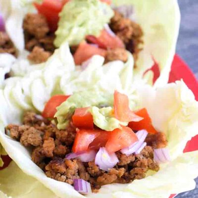 Cabbage leaf tacos sitting, ready to eat, on a red serving plate.