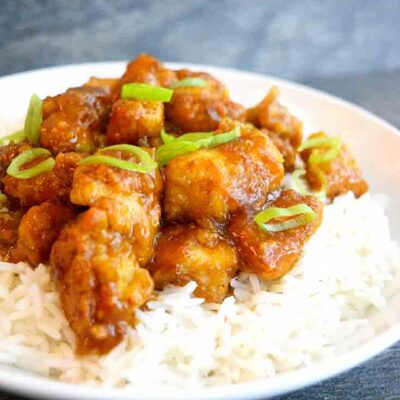 A front view of this bowl of Easy Orange Chicken topped with sliced green onions for garnish.