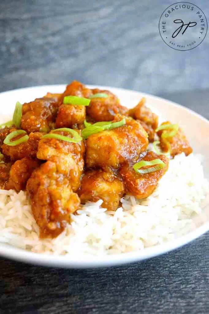 A front view of this bowl of Easy Orange Chicken topped with sliced green onions for garnish.