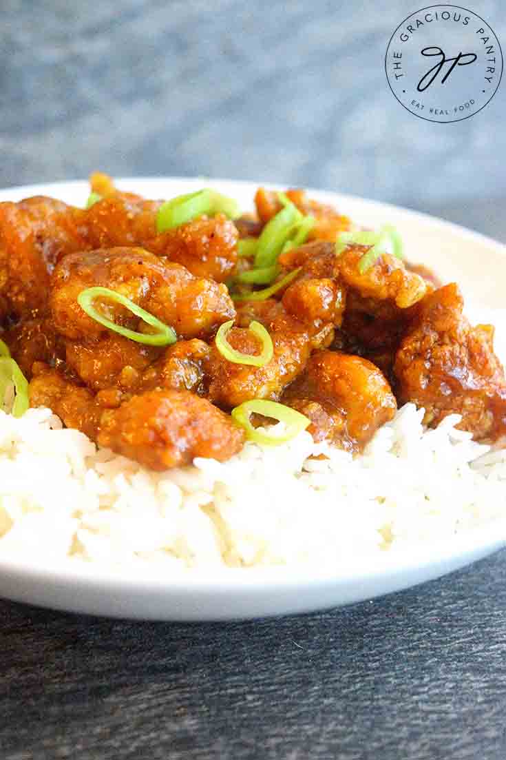 This Easy Orange Chicken sits on a bed of rice, served in a white bowl and topped with sliced, green onions.