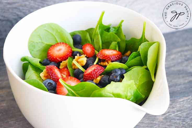 A tempting side view if this fresh spinach salad sitting on a table, ready and waiting for dressing.