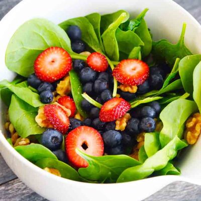 A side view of this delicious spinach salad recipe shows blueberries, sliced strawberries and walnuts layered in between the fresh spinach leaves.