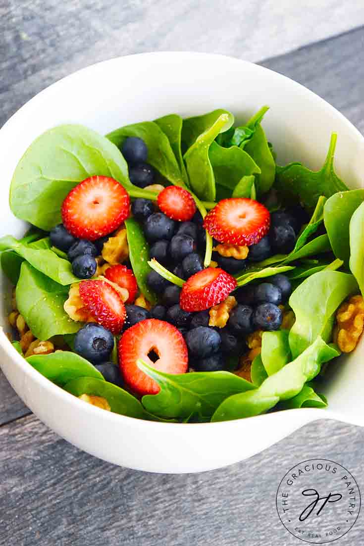 A side view of this delicious spinach salad recipe shows blueberries, sliced strawberries and walnuts layered in between the fresh spinach leaves.