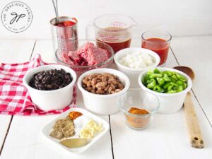 Several white bowls on a table filled with beef chili ingredients.