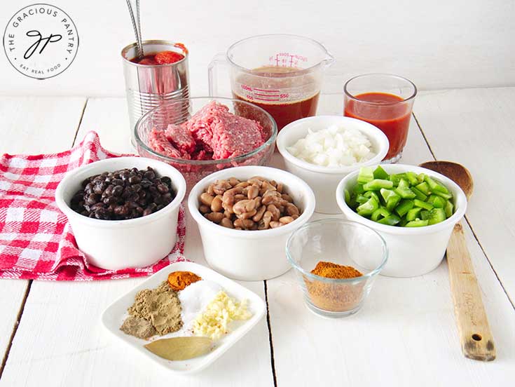 Several white bowls on a table filled with beef chili ingredients.