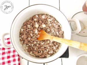 Browned beef in a pot with chopped onions added.