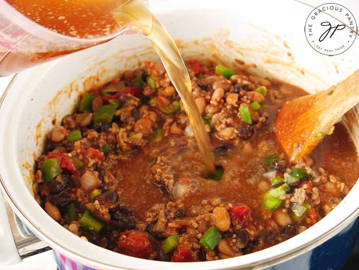 Broth being poured into a pot of beef chili.