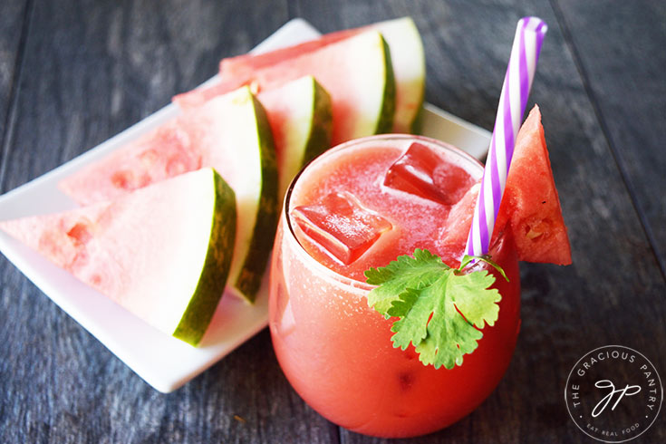 A glass of watermelon lemonade next to a platter of watermelon slices.