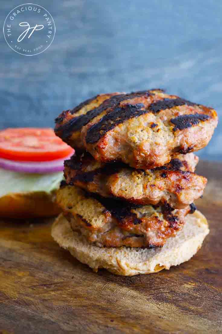 A stack of three Grilled Turkey Burgers sit on a whole grain but with the other half behind it loaded with lettuce, tomato and onion slices.