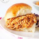 And up close shot of a prepared chicken slider sitting on a white plate, ready to eat.