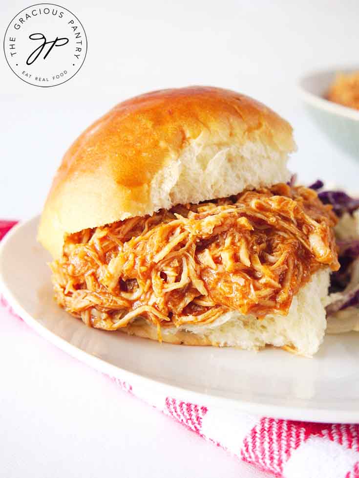 And up close shot of a prepared chicken slider sitting on a white plate, ready to eat.