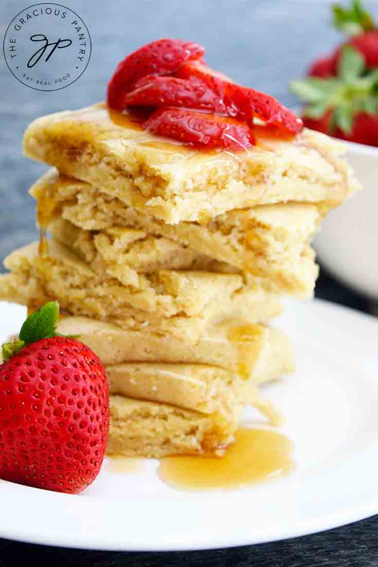 A stack of square, sheet pan pancakes sits piled high with strawberry slices and maple syrup on top.