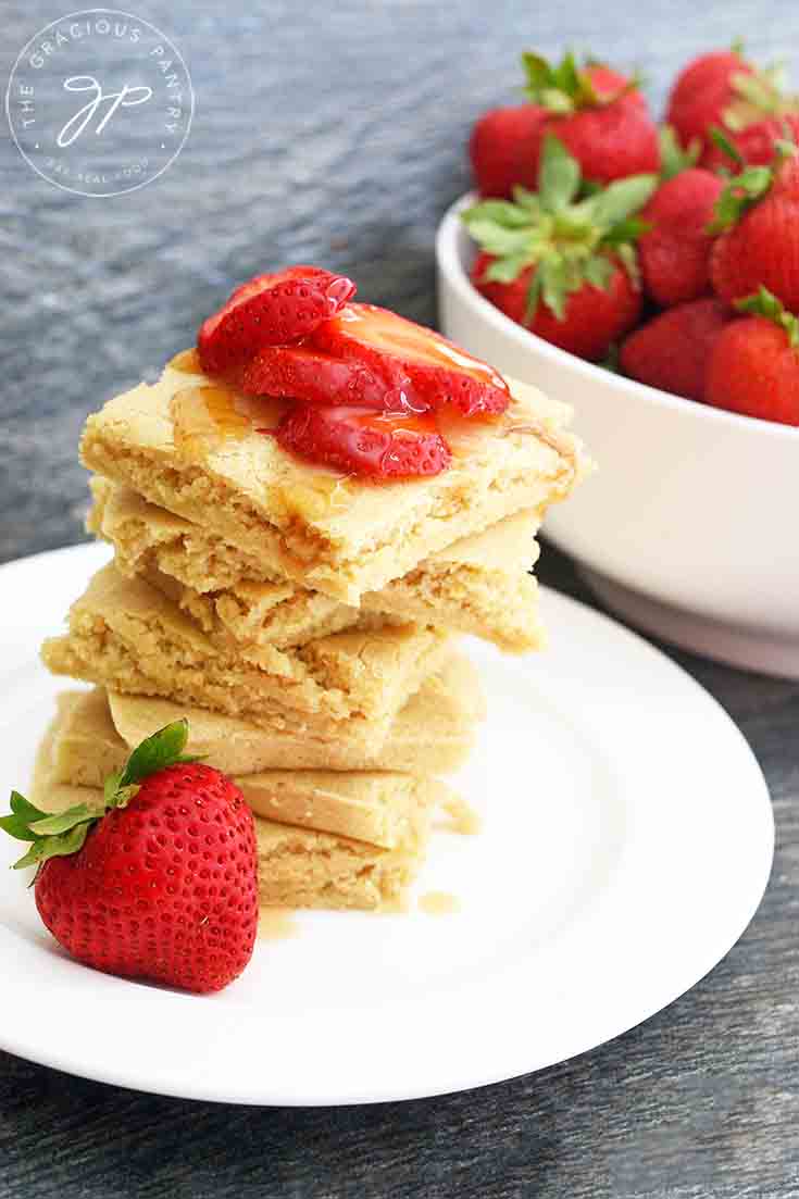 A larger view of a stack of these shee pan pancakes with a large bowl of strawberries sitting behind them.