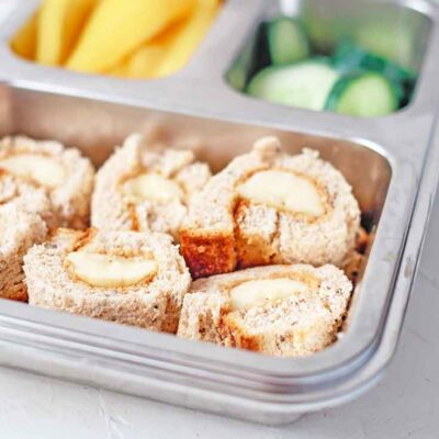 A side view of these Banana Nut Butter Sushi Rolls packed in a bento-style lunchbox.