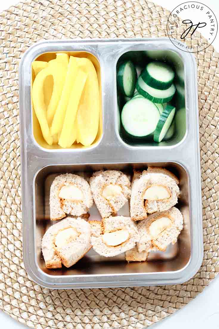 An overhead view of a bento style lunchbox packed with veggies and Banana Nut Butter Sushi Rolls.