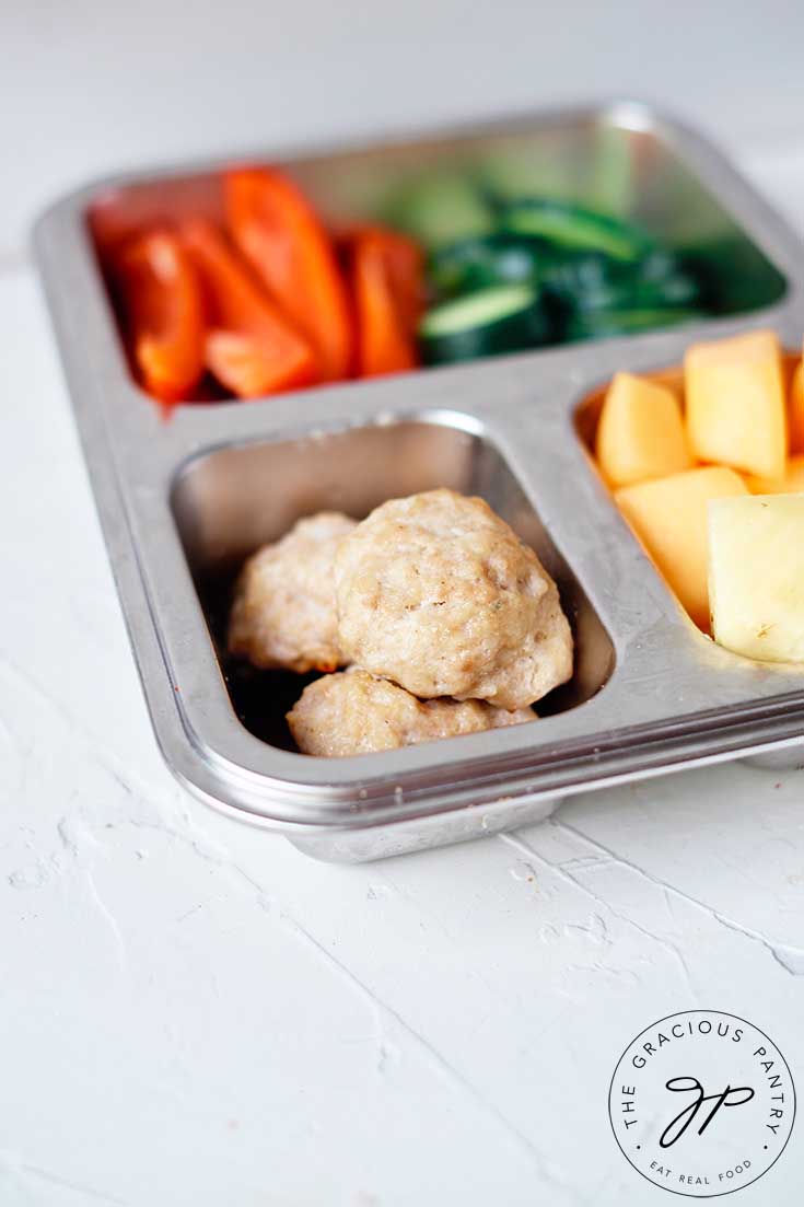 Chicken poppers, along with some cut veggies and fruit fill a bento style lunchbox.