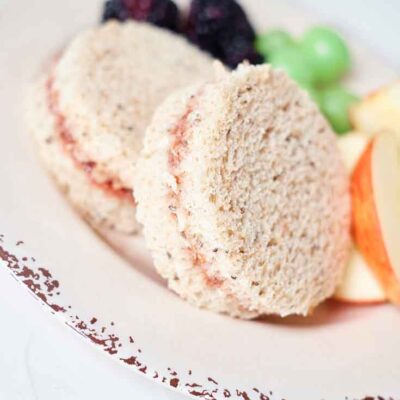 Two Jam Sandwiches on a plate with some cut fruit.