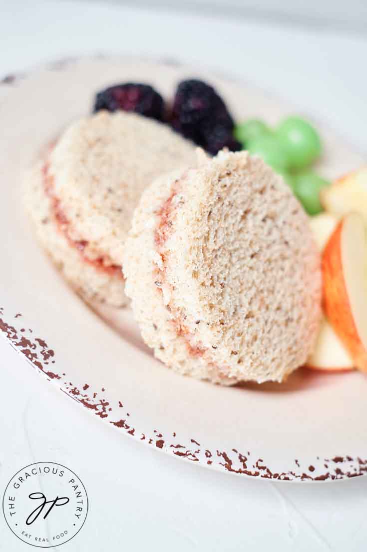 Two Jam Sandwiches on a plate with some cut fruit.