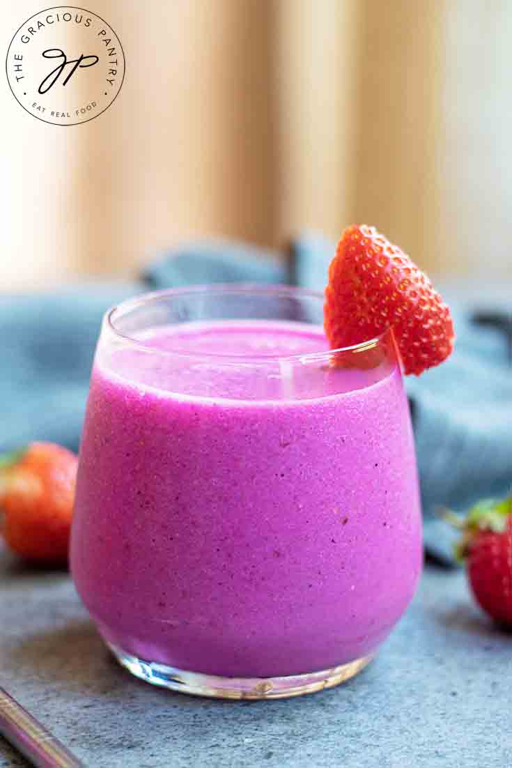 A single glass of pink dragon fruit smoothie with a strawberry on the rim.