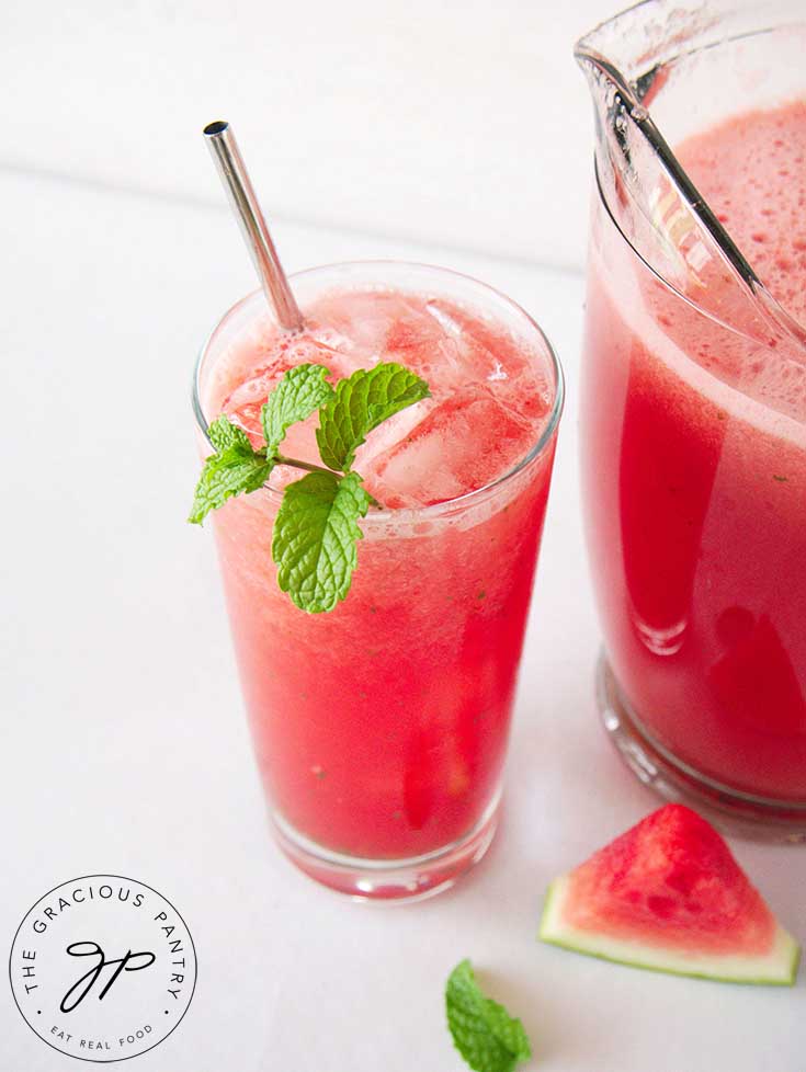 A full pitcher of Watermelon Agua Fresca With Mint sits next to the glass it just filled.