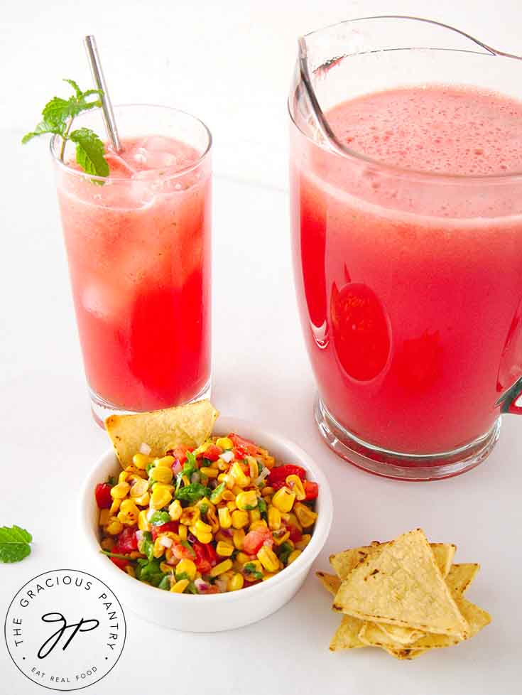 A pitcher and glass both filled, and a bowl of corn salsa with corn chips sitting next to them.