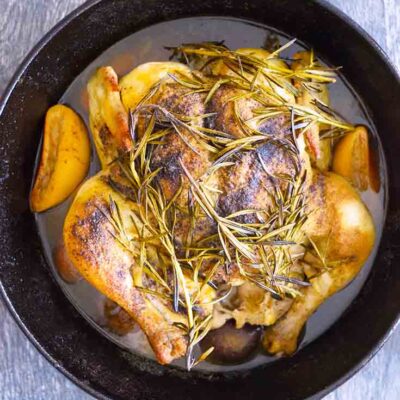 Vertical, overhead view looking down into a cast iron dutch oven with a cooked, dutch oven whole chicken in it.