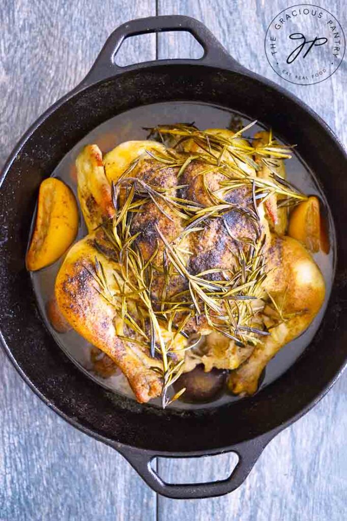 Vertical, overhead view looking down into a cast iron dutch oven with a cooked, dutch oven whole chicken in it.