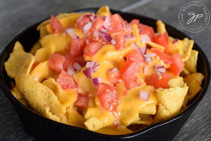 A black skillet filled with chips covered in nacho cheese sauce and topped with chopped tomatoes and chopped onions.
